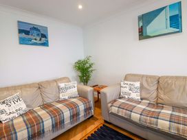 A living room with two beige sofas covered with plaid throws and cushions a wooden side table with a plant between the sofas and paintings on white walls at Pink House in Mevagissey