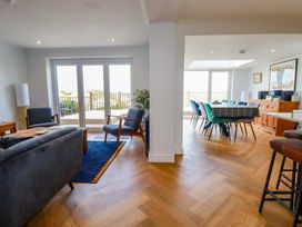 A living room with chairs and a couch next to glass doors leading to a patio and a dining area with a long table and chairs at Pink House Mevagissey