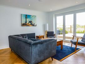 A living room with gray sofa and chairs a wooden coffee table a painting of a lighthouse on wall and glass doors leading to a balcony at Pink House in Mevagissey