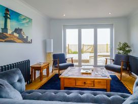 A living room with blue armchairs a wooden coffee table and a lighthouse painting on the wall at Pink House in Mevagissey