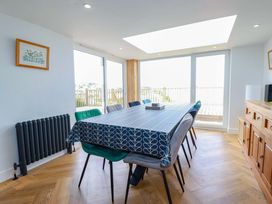 A dining room with a table covered by a blue patterned tablecloth surrounded by chairs and large windows at Pink House in Mevagissey