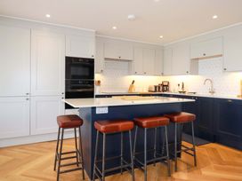 A kitchen with white and dark blue cabinets a white countertop an island with four brown stools and wooden flooring at Pink House in Mevagissey