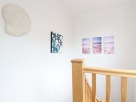 A stairway with wooden railing and wall art including a large shell and photos of the beach at Pink House Mevagissey