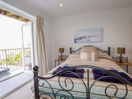 A bedroom with a metal bed frame two bedside tables with lamps and a door leading to a balcony at Pink House in Mevagissey