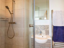 A bathroom with a shower area with a handheld showerhead a sink with a patterned tile backsplash and towels hanging on a towel rack at Pink House in Mevagissey
