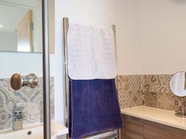 A bathroom with patterned tiles a towel rack holding white and purple towels a sink and a round mirror at Pink House in Mevagissey