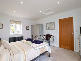 A bedroom with a double bed striped bedding a wardrobe a bench with cushions a wooden door and a window with striped blinds at Pink House in Mevagissey