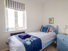 A bedroom with a blue bed and bedding near a window with striped blinds and a blue dresser with a lamp at Pink House in Mevagissey