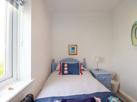 A small bedroom with a single bed a blue bedside table lamp and a window with striped curtains at Pink House in Mevagissey