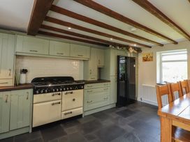 A kitchen with cabinets, stove, refrigerator, and dining table at Plas Mawr in Groeslon
