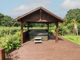 A wooden gazebo with a hot tub on a deck at Beudy'r Wennol in Groeslon