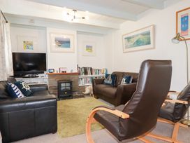 A living room with black leather sofas a green rug a wooden armchair a small heater and framed pictures on the walls at Daisy Cottage in Perranporth