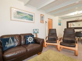 A living room with a brown leather sofa with nautical pillows two black chairs wooden door wall art and a large mirror at Daisy Cottage in Perranporth
