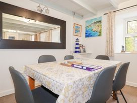 A dining room with a table covered by a patterned tablecloth surrounded by six chairs and a large wall mirror at Daisy Cottage in Perranporth