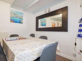 A dining room with a table covered with a patterned tablecloth surrounded by chairs and a large mirror on the wall at Daisy Cottage in Perranporth
