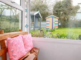 A wooden bench with pink flamingo cushions next to a window overlooking a garden with flowers and a colorful striped shed at Daisy Cottage in Perranporth