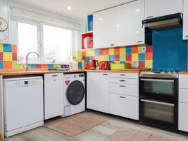 A kitchen with white cabinets colorful tiled backsplash washer dishwasher oven and kettle at Daisy Cottage in Perranporth