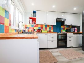 A kitchen with white cabinets wooden countertops colorful tiled walls and appliances at Daisy Cottage in Perranporth