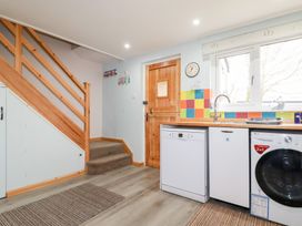 A kitchen area with appliances under a counter next to a wooden staircase and a wooden door at Daisy Cottage in Perranporth