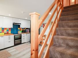 A kitchen with white cabinets a colorful tiled backsplash and a carpeted staircase with wooden railing at Daisy Cottage in Perranporth