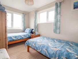 A bedroom with two single beds blue bird-patterned bedding wooden chest of drawers and a nightstand with a lamp at Daisy Cottage in Perranporth