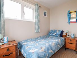 A bedroom with a single bed with bird patterned bedding two wooden bedside tables with lamps and a window with patterned curtains at Daisy Cottage in Perranporth