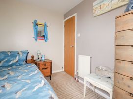 A bedroom with a wooden door a small wooden chest a bed with bird patterned bedding a white bench and a tall wooden dresser at Daisy Cottage in Perranporth