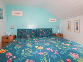 A bedroom with a bed with floral bedding two bedside tables with lamps and framed pictures on the walls at Daisy Cottage in Perranporth