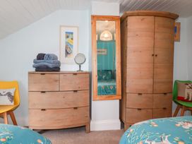 A bedroom corner with wooden dresser and wardrobe a wall mirror and two chairs with cushions at Daisy Cottage in Perranporth