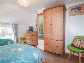 A bedroom with two beds blue bedding wooden dresser wooden wardrobe and green chair with dog cushion at Daisy Cottage in Perranporth