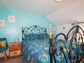 A bedroom with a black metal bed frame and floral bedding a wooden nightstand with a lamp and blue chair at Daisy Cottage in Perranporth