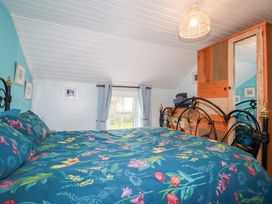 A bedroom with a floral bedspread a wooden wardrobe a small window and light blue walls at Daisy Cottage in Perranporth
