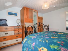 A bedroom with a black metal bed frame a floral bedspread a wooden dresser with folded towels and a mirror and a wooden wardrobe at Daisy Cottage in Perranporth