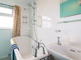 A bathroom with a bathtub a shower sink and a window with a curtain at Daisy Cottage in Perranporth