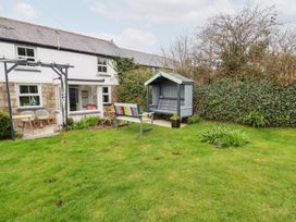 A garden with a house patio, two chairs, a colorful bench, a covered wooden swing, and bushes at Daisy Cottage in Perranporth