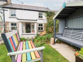 A garden area with a colorful bench and a covered gray bench in front of a white house with windows at Daisy Cottage in Perranporth