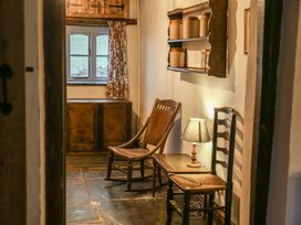 A hallway with wooden chairs a small table with a lamp a wooden shelf holding jars and a window with floral curtains at Pant Dafydd Goch in Llangollen