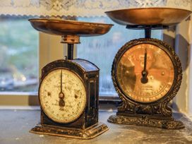 Two vintage kitchen scales on a windowsill with lace curtains in the background at Pant Dafydd Goch in Llangollen