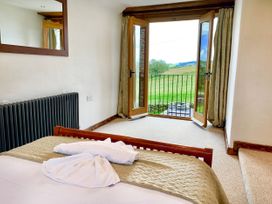 A bedroom with a bed a large mirror on the wall a radiator and open doors leading to a balcony with a view of green fields at Pant Dafydd Goch in Llangollen