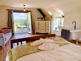 A bedroom with a bed, sofa, chest of drawers, freestanding bathtub, and open door leading to a balcony with table and chairs at Pant Dafydd Goch in Llangollen