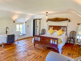 A bedroom with a wooden bed two chairs freestanding bathtub and a full length mirror at Pant Dafydd Goch in Llangollen