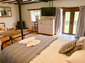A bedroom with a bed near glass doors and curtains a chest of drawers with a wall mounted tv and a wood stove at Pant Dafydd Goch in Llangollen