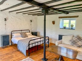 A bedroom with a metal bed frame sofa wooden table wooden floor and white stone walls at Pant Dafydd Goch in Llangollen