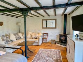 A room with a beige sectional sofa with cushions a wooden coffee table a black wood burning stove a wooden chair a white dresser with a clock and a television on top a patterned rug and wooden floors at Pant Dafydd Goch in Llangollen