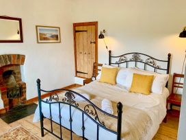 A bedroom with a metal bed frame two yellow pillows a wooden floor and a small fireplace at Pant Dafydd Goch in Llangollen