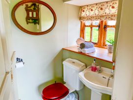 A small bathroom with a toilet with a red seat cover a white sink a wooden window sill with folded towels a plant and a round mirror on the wall at Pant Dafydd Goch in Llangollen