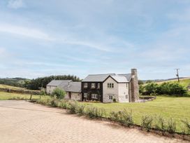 A country house with a stone chimney and a paved driveway surrounded by grass and bushes at Pant Dafydd Goch in Llangollen