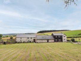 A long stone and wood house with a lawn and hills in the background at Pant Dafydd Goch in Llangollen