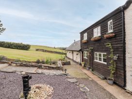 Exterior view of a house with wooden and stone walls overlooking a garden with stone pathways and green fields at Pant Dafydd Goch in Llangollen