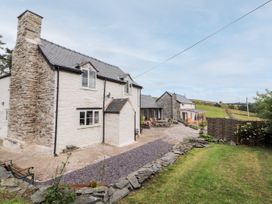 A stone and white plaster house with a paved patio and outdoor furniture next to a grassy yard at Pant Dafydd Goch in Llangollen